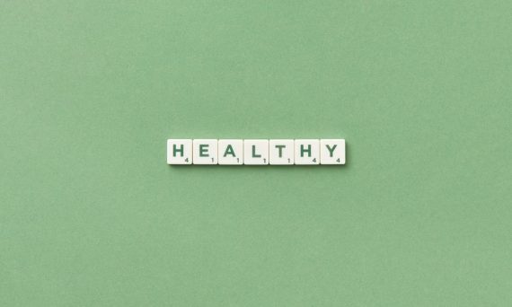 Scrabble tiles spelling the word 'healthy' on a light green background, top view.